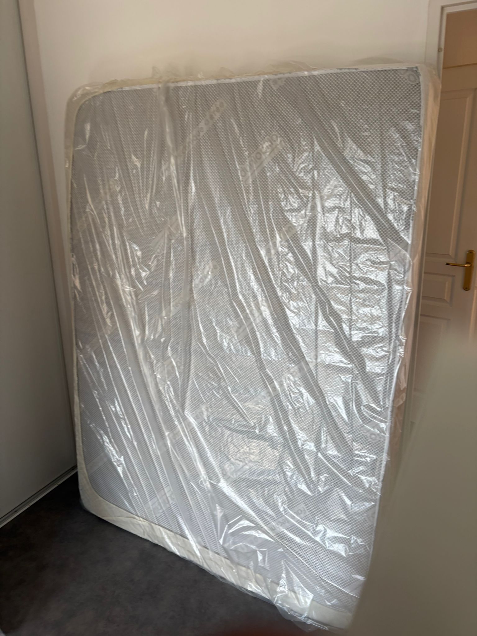Matelas emballé sous film dressé dans un couloir avant enlèvement